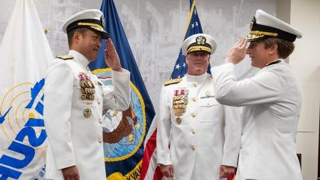 Three individuals in Naval uniforms saluting one another.